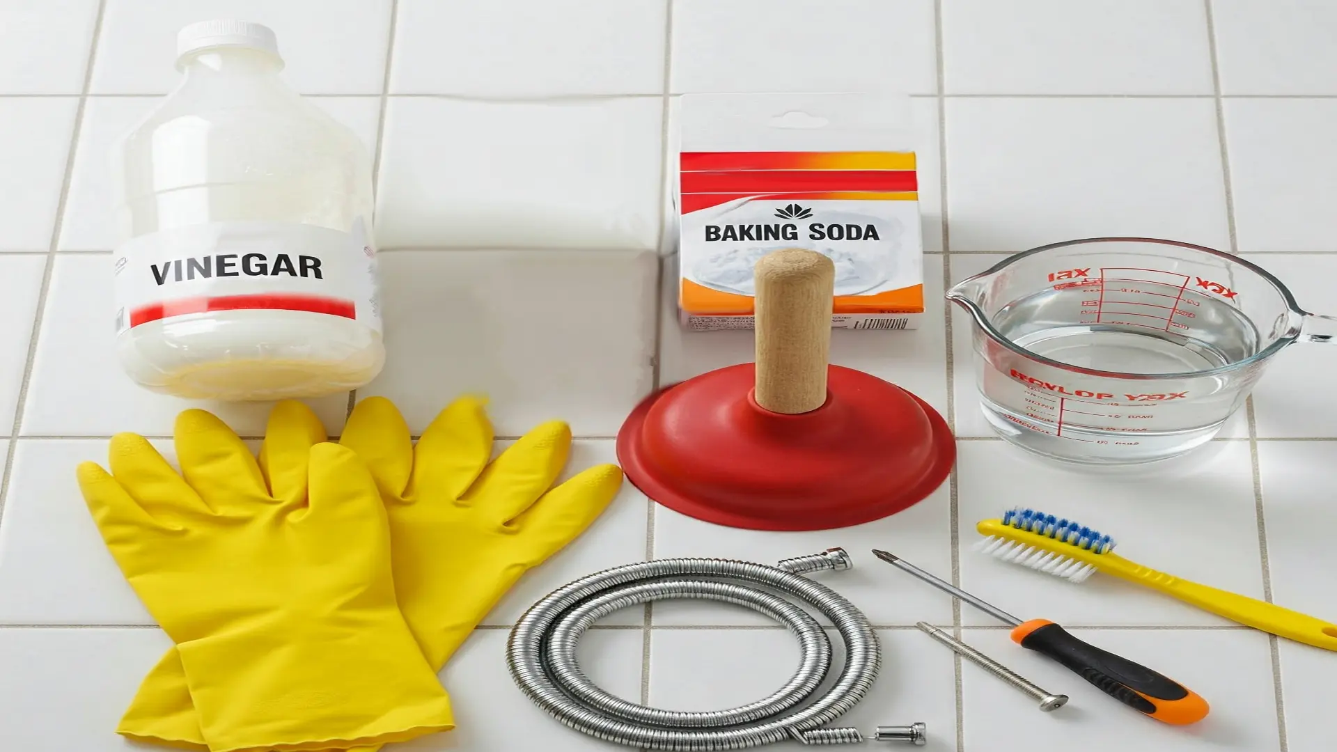 Various tools and household items laid out for unclogging a shower drain, including pliers, a drain snake, and a cleaning solution.